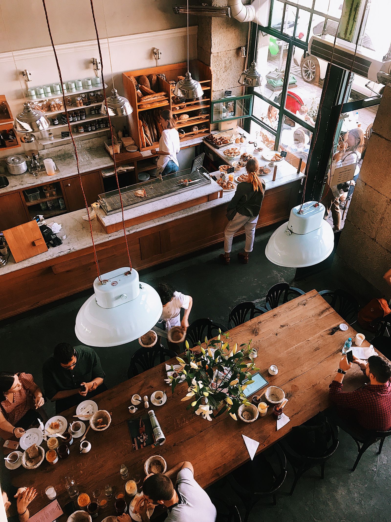 A long communal table in a bakery, neighbours sharing coffee and bread